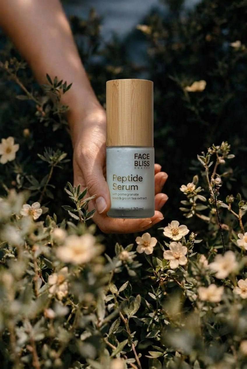 Hand holding a Face Bliss Peptide Serum bottle against a natural background with flowers.